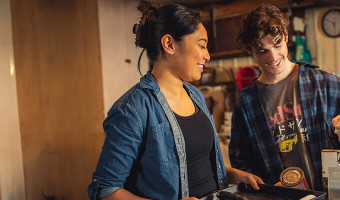 A man and woman are standing together in a garage holding up painting supplies and smiling