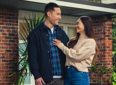 A man and women are standing in front of a home looking towards each other and smiling