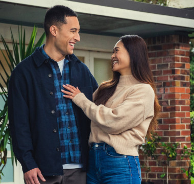 A man and women are standing in front of a home looking towards each other and smiling