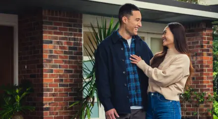 A man and women are standing in front of a home looking towards each other and smiling