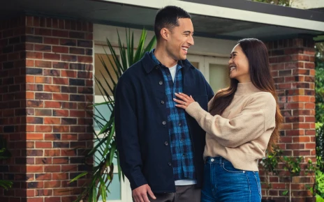 A man and women are standing in front of a home looking towards each other and smiling