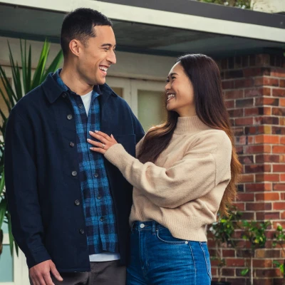 A man and women are standing in front of a home looking towards each other and smiling
