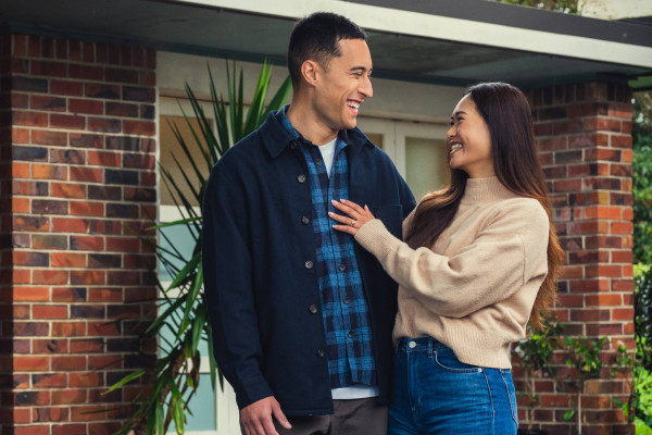 A man and women are standing in front of a home looking towards each other and smiling