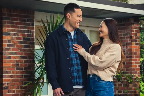 A man and women are standing in front of a home looking towards each other and smiling