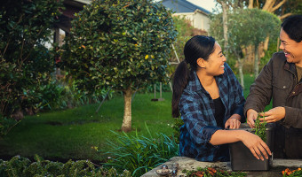 Two women are standing together outside and gardening. They are looking at each other and laughing.