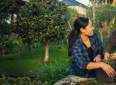 Two women are standing together outside and gardening. They are looking at each other and laughing.