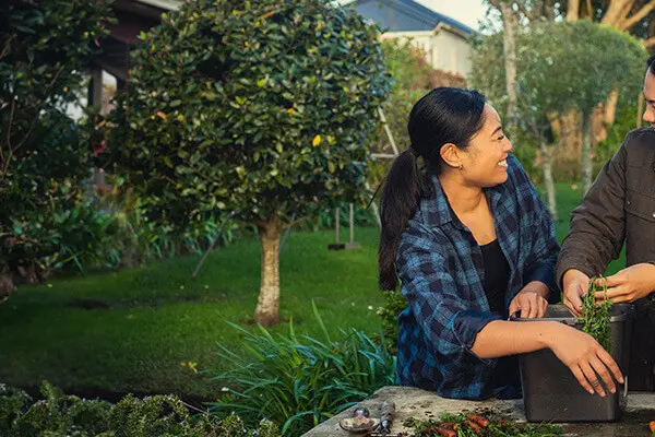 Two women are standing together outside and gardening. They are looking at each other and laughing.