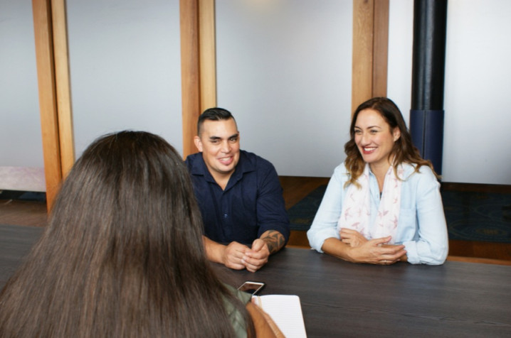 Couple smiling talking to woman over a desk