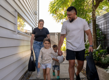 A family of four, two adults and two children, walking hand in hand beside a house.