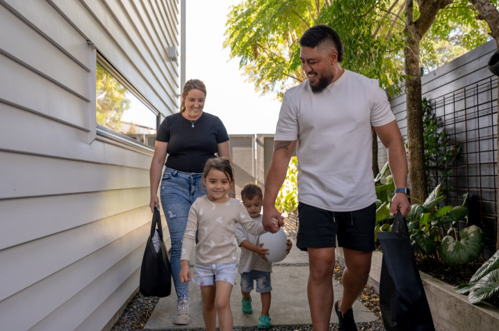 A family of four, two adults and two children, walking hand in hand beside a house.
