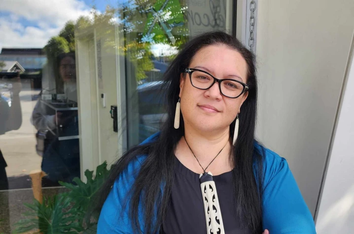 Indigo Phillips standing outside a building, wearing a blue jacket and pendant, representing a Māori woman sharing her homeownership journey with Sorted Kāinga Ora. 