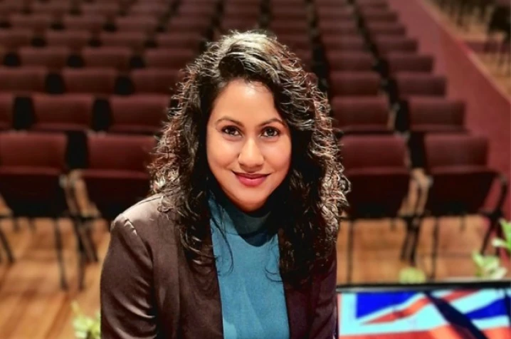 Shristi looking at the camera in a theater holding her certificate of NZ citizenship.