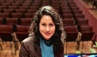Shristi looking at the camera in a theater holding her certificate of NZ citizenship.