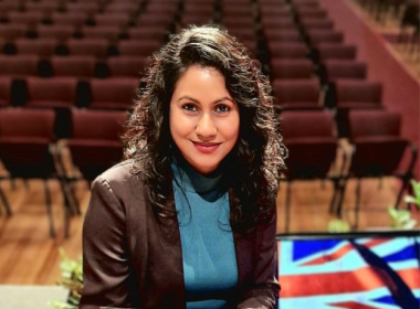 Shristi looking at the camera in a theater holding her certificate of NZ citizenship.