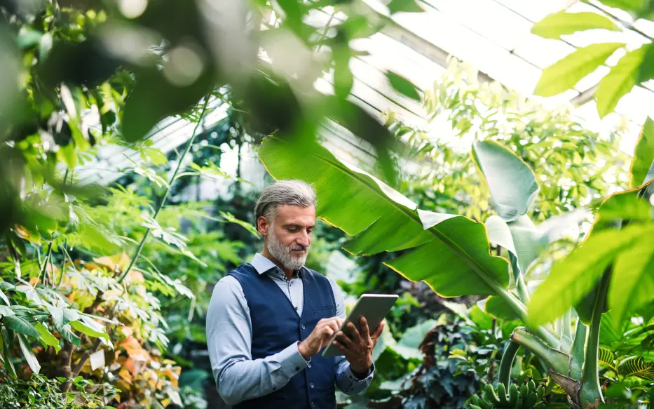 Man holding a tablet in a winter garden surrounded by plants