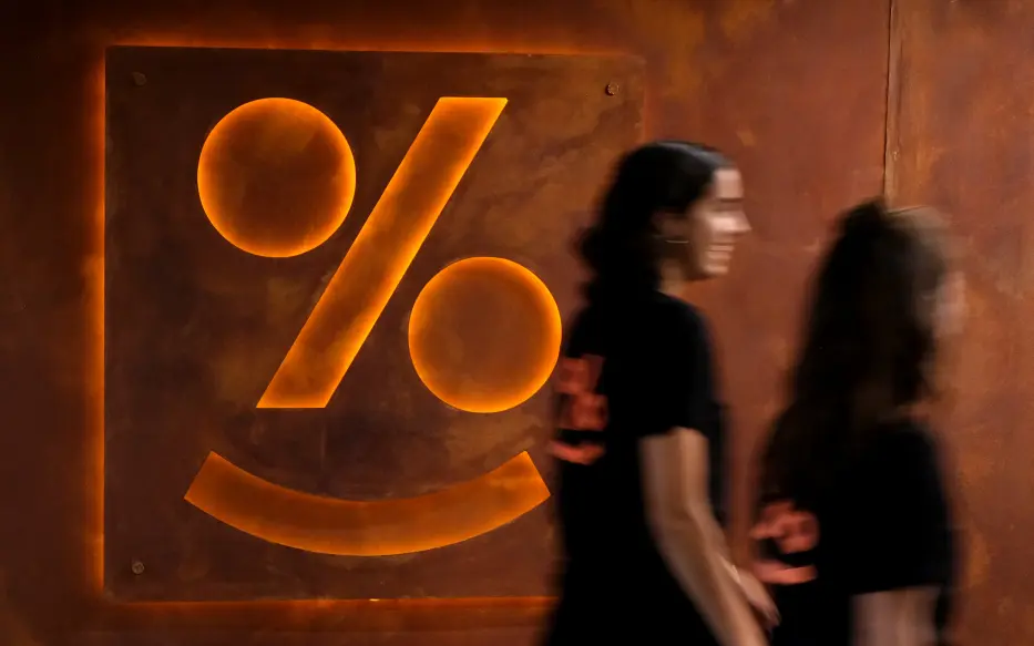 Two people blurred by movement walking past a Simplicity logo on the wall.