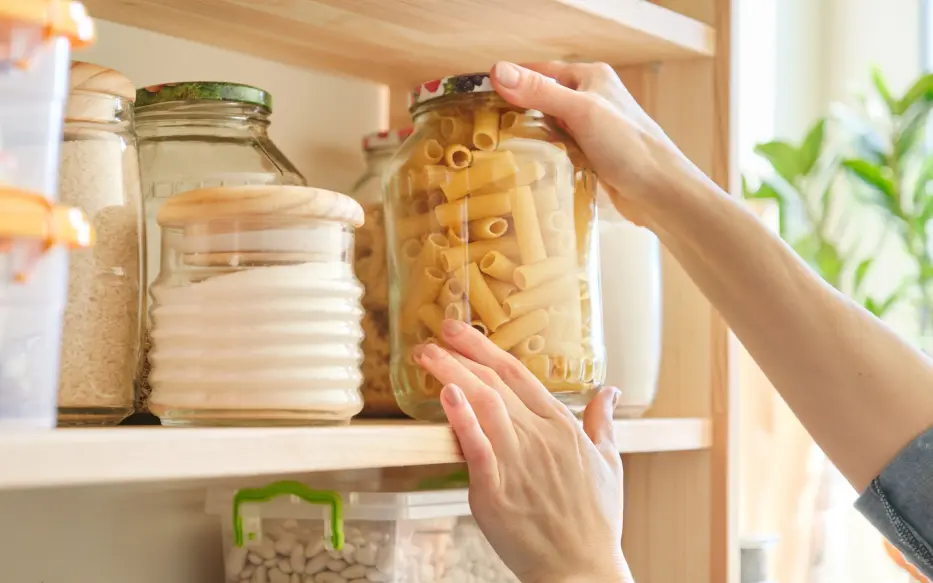 Close up of pantry with staples, and a hand grabbing a packet of pasta